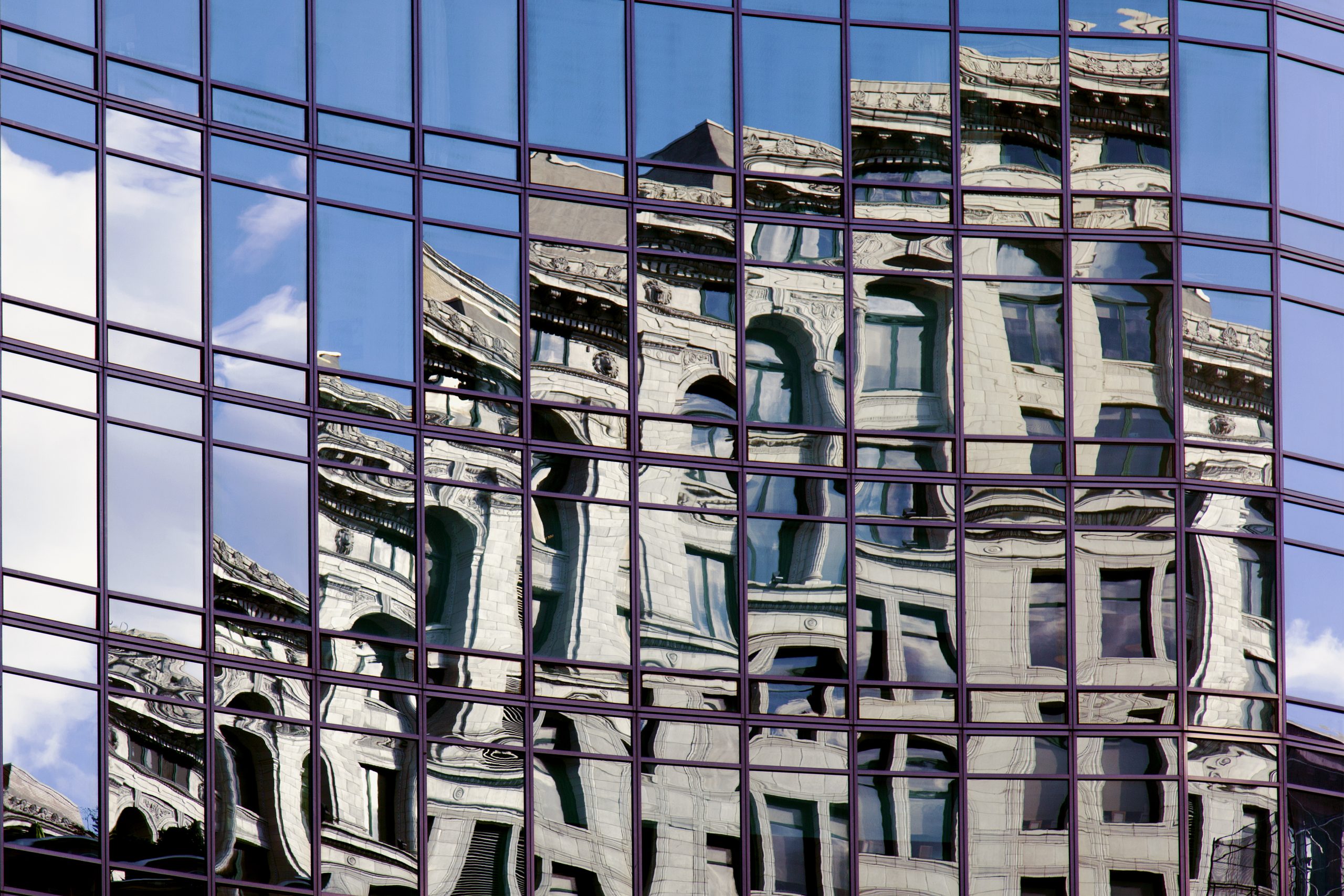 An abstract reflection of a historic London building on mirrored glass windows with blue sky.