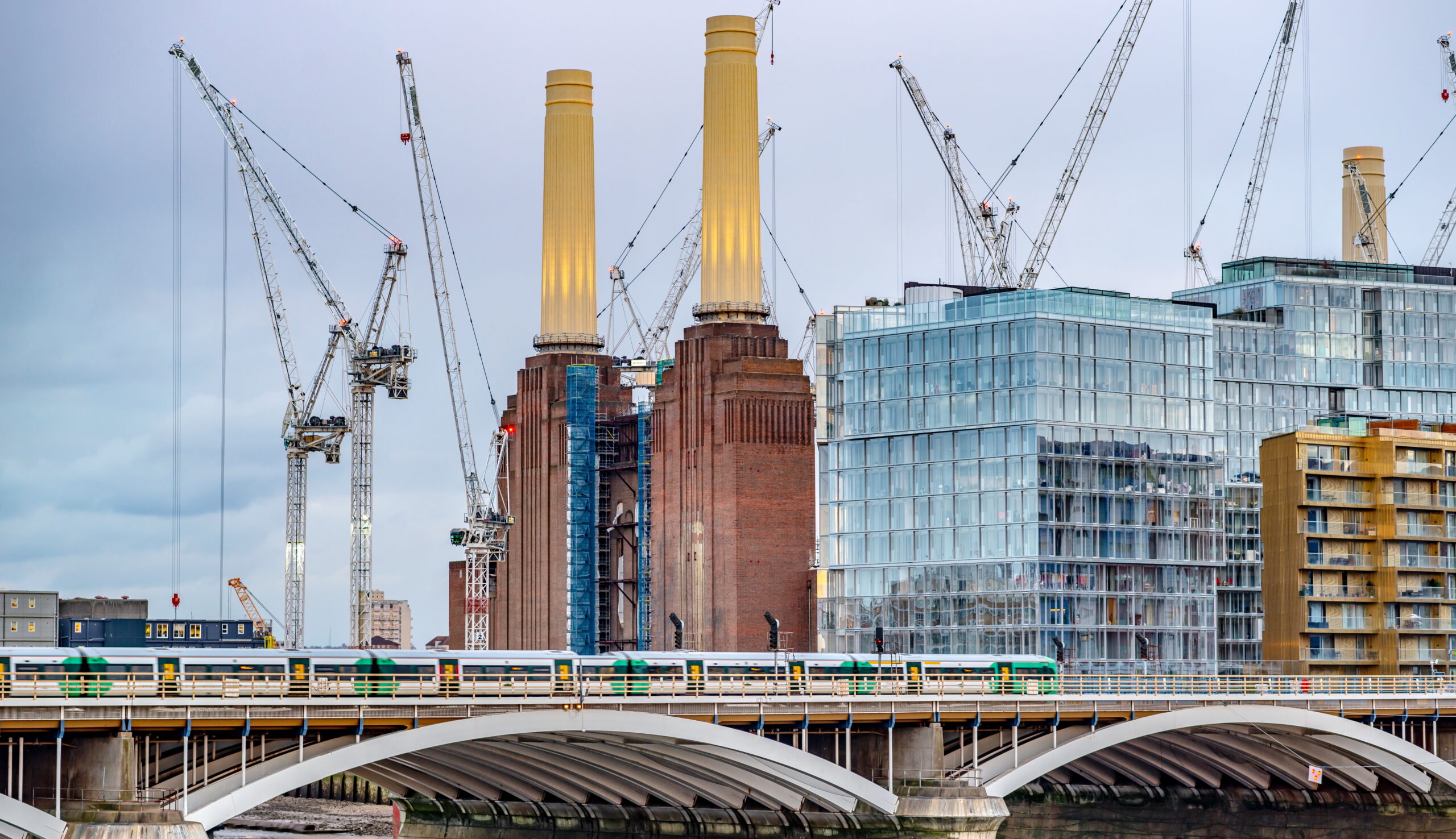 A photo of Battersea Power Station, London, surrounded by cranes with a railway bridge in the foreground.