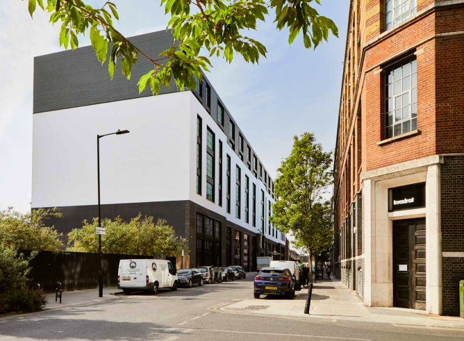 A side perspective of the Wenlock Works building in Old Street painted in black and grey with green trees and bushes in the frame.